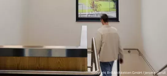 Treppenhaus aus Holz und Metall mit Person, die die Treppe heruntergeht